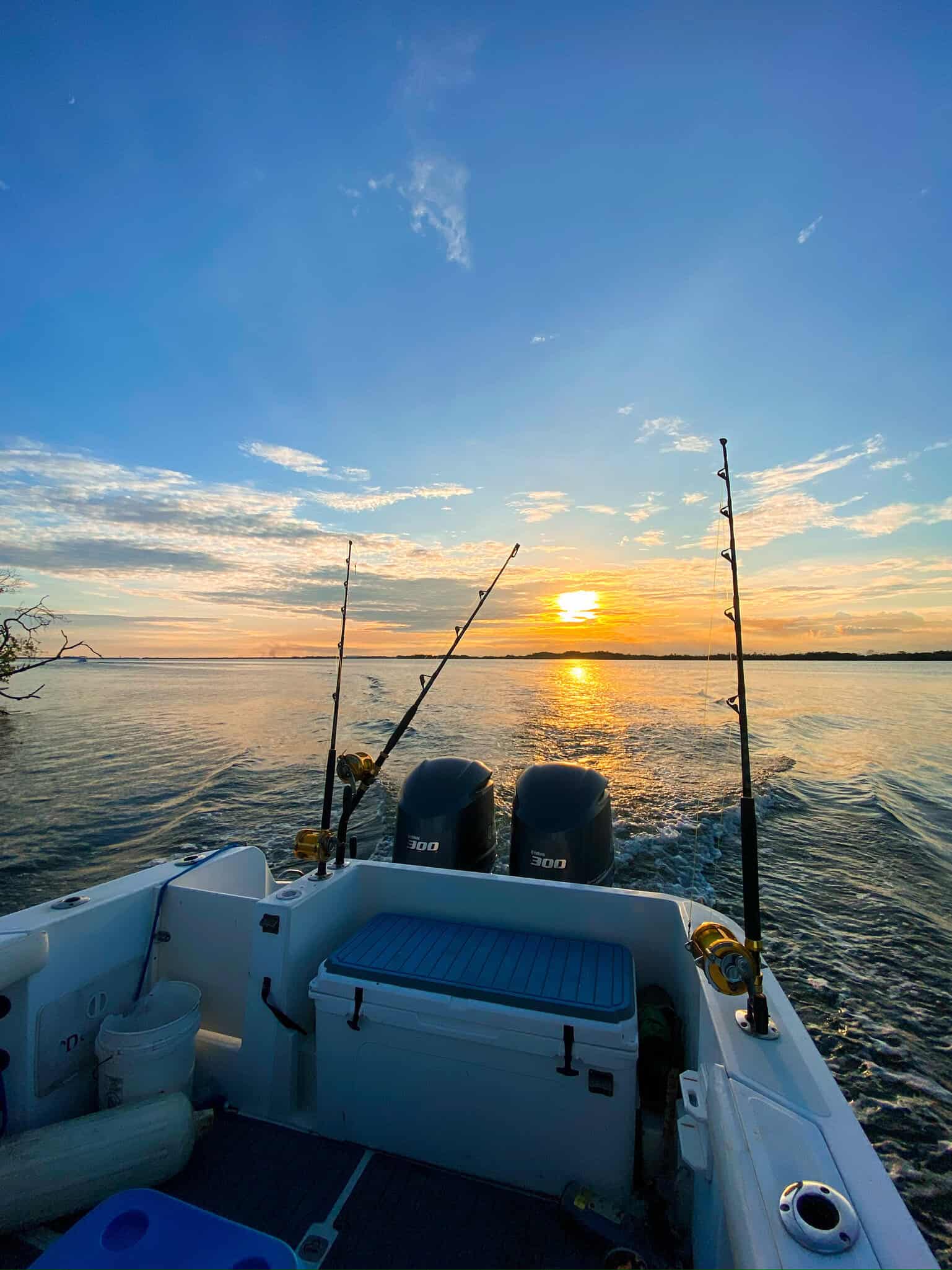 Deep sea fishing boat on Belize reef with sunset in the background, twin outboard motors, fishing rods, and calm ocean waters, offering premium Belize Reef Charters for fishing adventures.