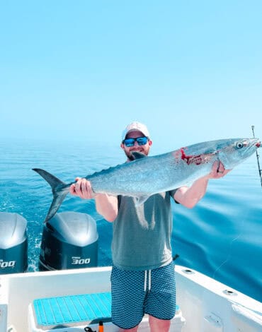 Vibrant Caribbean sea fishing with a man holding a large, freshly caught fish on a boat in Belize. Perfect for showcasing Belize Reef Charters' fishing adventures.