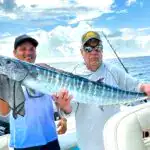 Vibrant longtail marlin fishing in Belize with anglers on a charter boat under a partly cloudy sky.