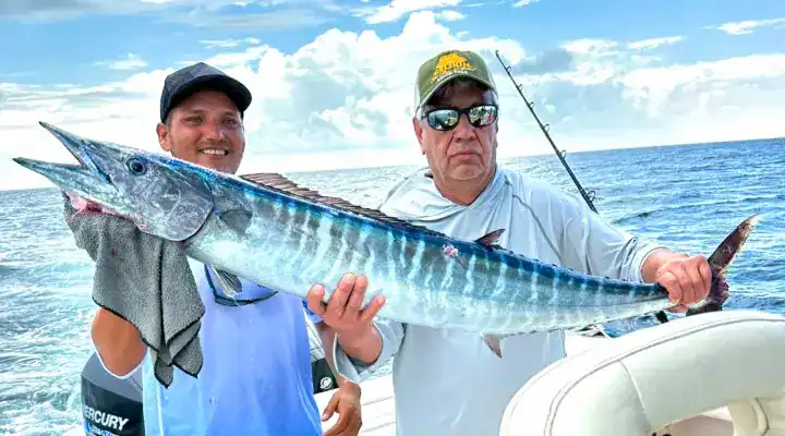 Vibrant longtail marlin fishing in Belize with anglers on a charter boat under a partly cloudy sky.