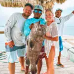 Large group of people holding a big fish after a successful Belize reef fishing trip, showcasing the excitement of Belize Reef Charters and offshore fishing adventures.